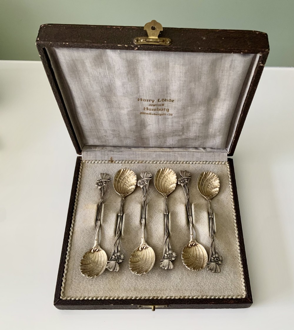 A set of six Art Nouveau silver teaspoons with shell bowls and floral stems, displayed inside an open fitted cloth-lined presentation box.