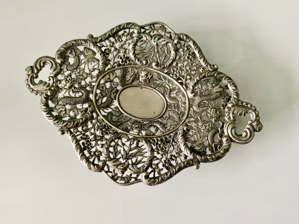 An oval Chinese export silver dish featuring pierced openwork decorated with chased dragons, bamboo foliage, and integrated side handles.