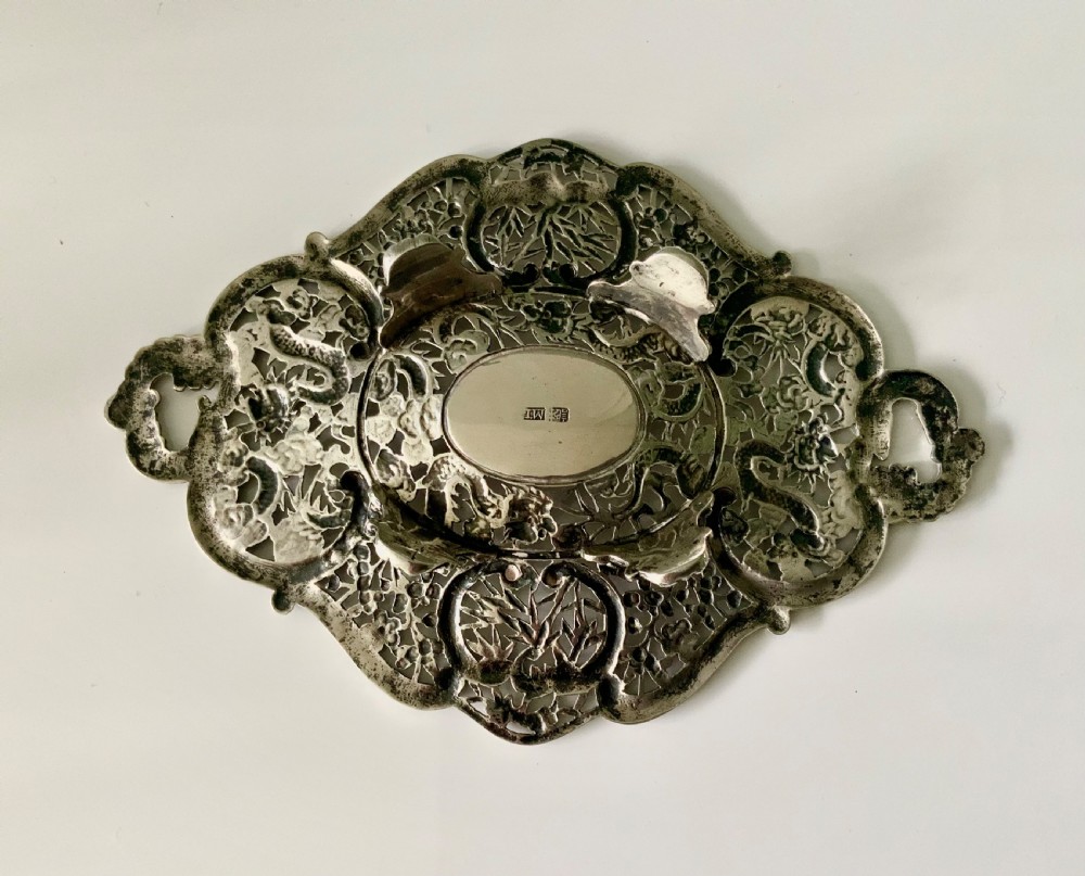 An oval Chinese export silver dish featuring pierced openwork decorated with chased dragons, bamboo foliage, and integrated side handles. View III