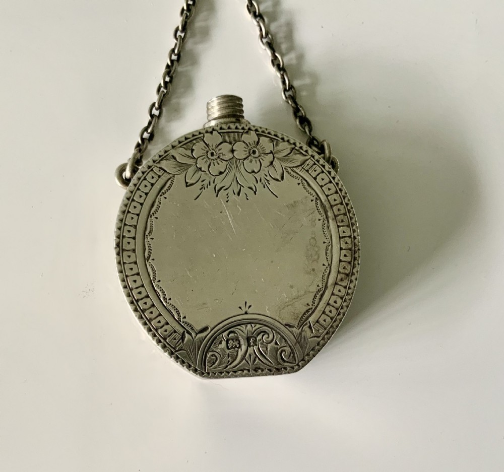 A circular silver and green Connemara marble perfume bottle with a central shamrock motif, suspended from a chain and ring. View V