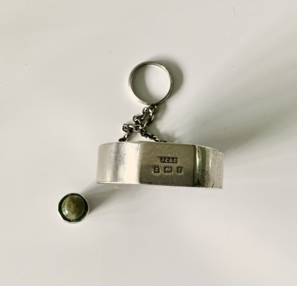 A circular silver and green Connemara marble perfume bottle with a central shamrock motif, suspended from a chain and ring. View VI