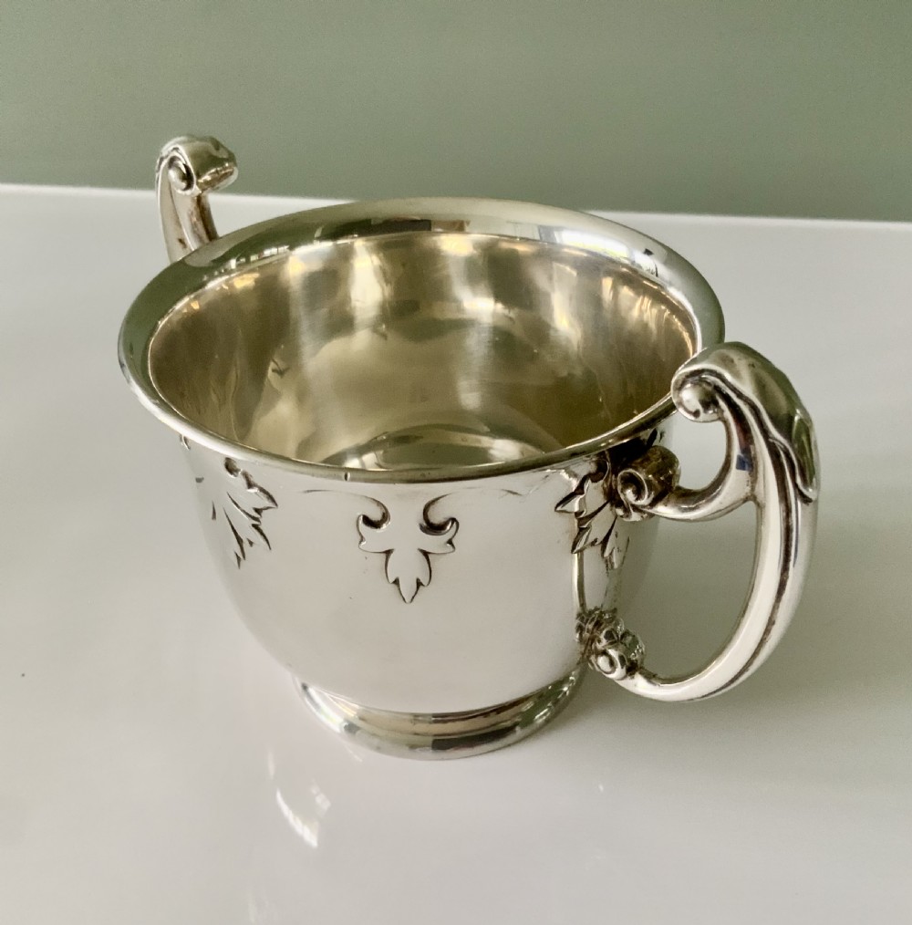 A polished silver loving cup featuring two prominent scroll handles and embossed leaf detailing around the body.