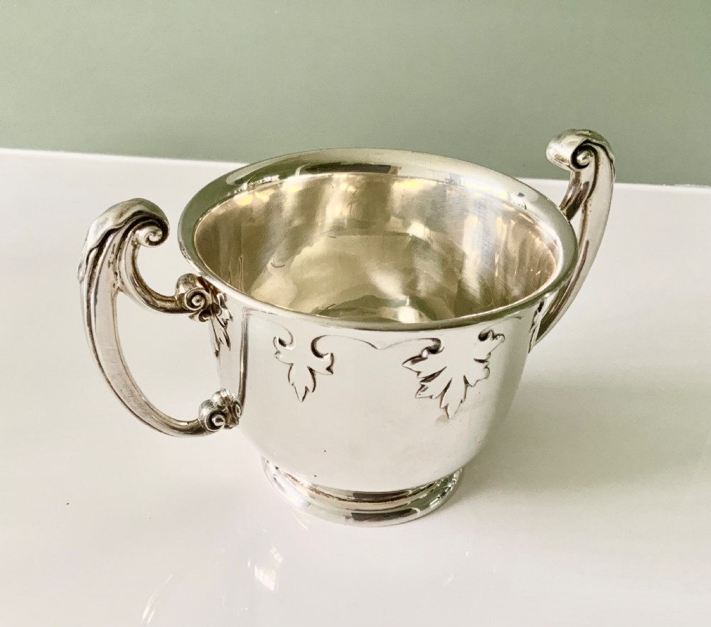 A polished silver loving cup featuring two prominent scroll handles and embossed leaf detailing around the body. View II