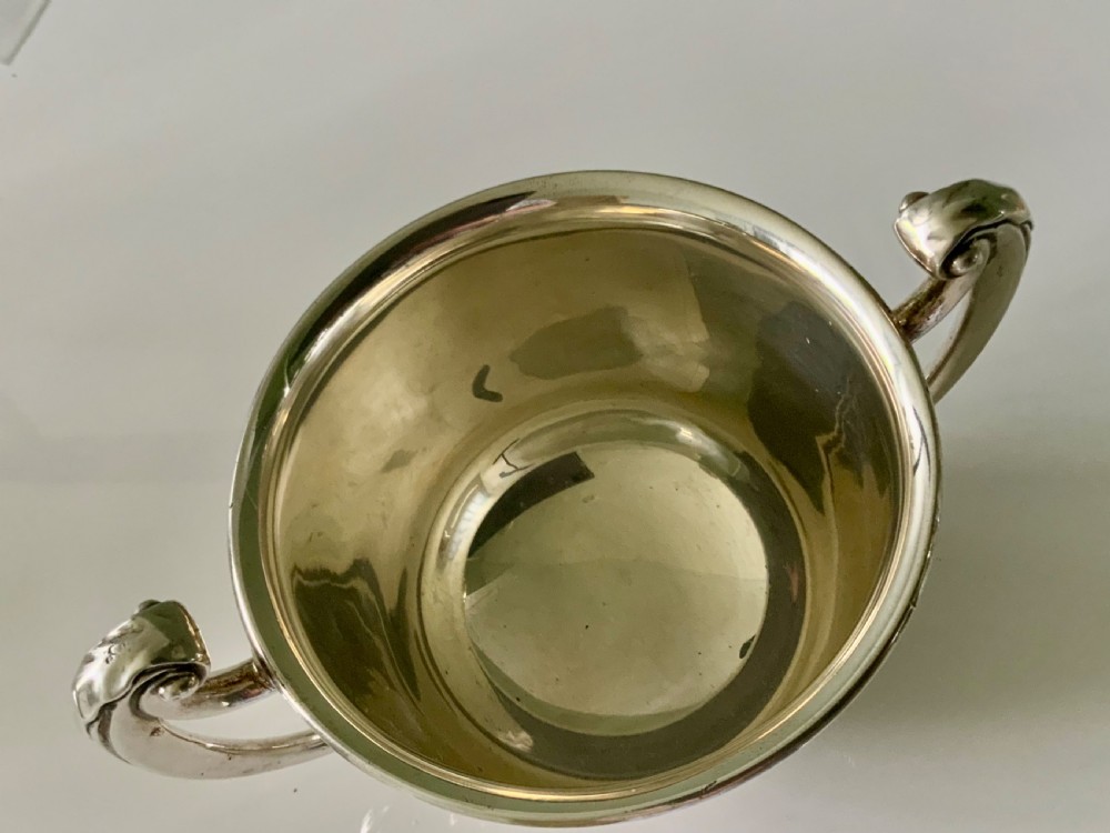 A polished silver loving cup featuring two prominent scroll handles and embossed leaf detailing around the body. View IV