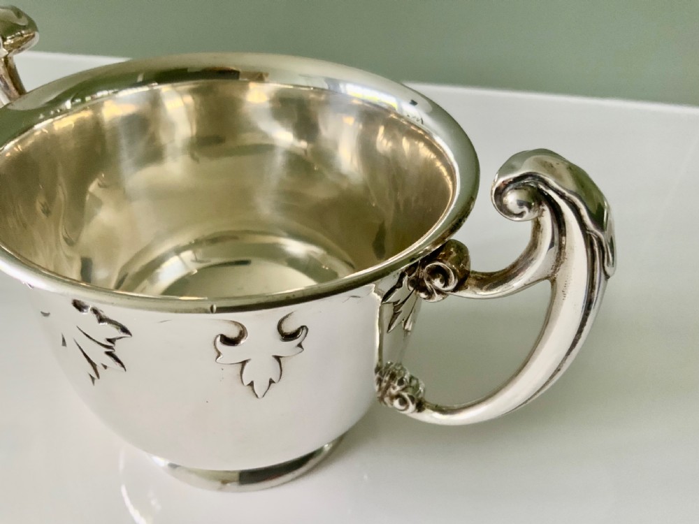 A polished silver loving cup featuring two prominent scroll handles and embossed leaf detailing around the body. View VI