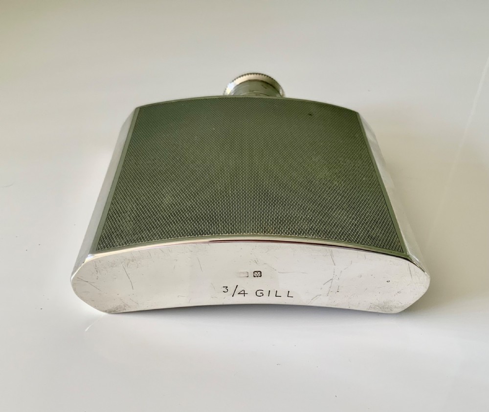 An Art Deco silver hip flask featuring a subtle engine-turned pattern, a contoured body, and a hinged bayonet cap engraved with an emblem. View VI