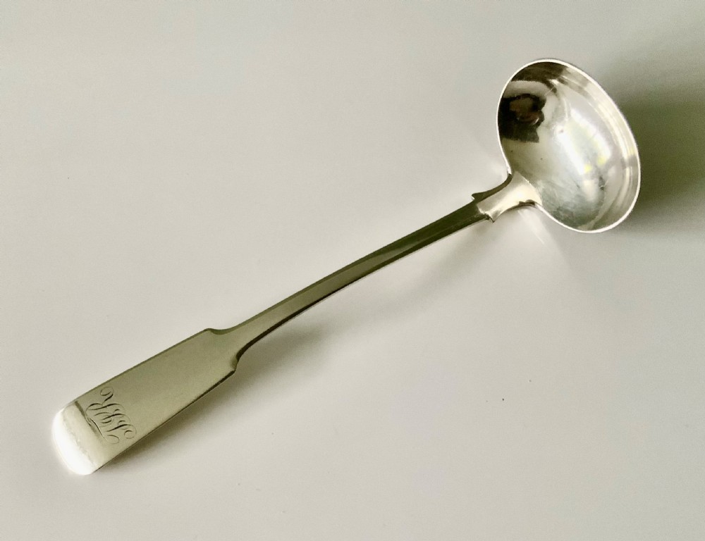 A silver toddy ladle featuring a rounded circular bowl and a fiddle pattern stem with engraved monogram initials.