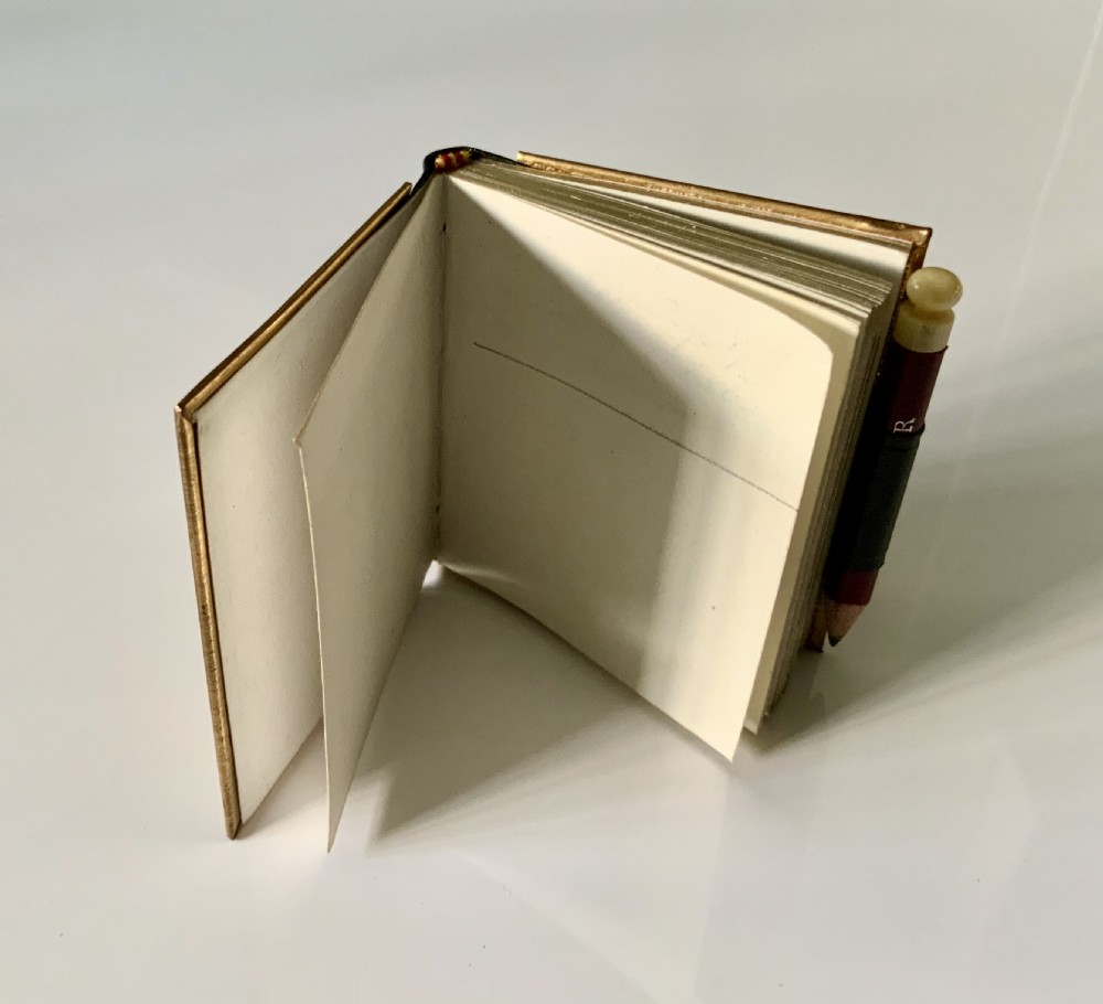 A late nineteenth-century miniature notebook featuring an embossed brass front cover with floral scrollwork, a dark leather spine, and an attached pencil. View IV