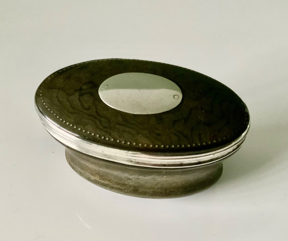 An oval antique Scottish snuff mull with a dark horn body and a fitted silver-mounted lid featuring an inset blank shield.