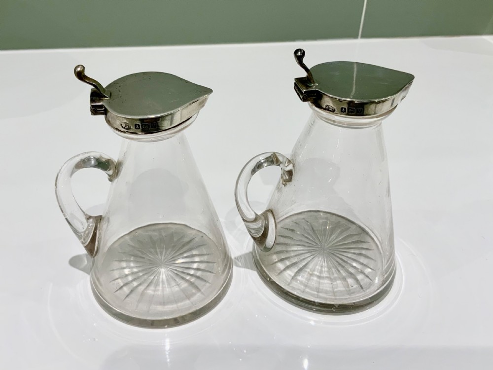 A pair of conical clear glass whisky noggins with star-cut bases and hallmarked sterling silver hinged lids.