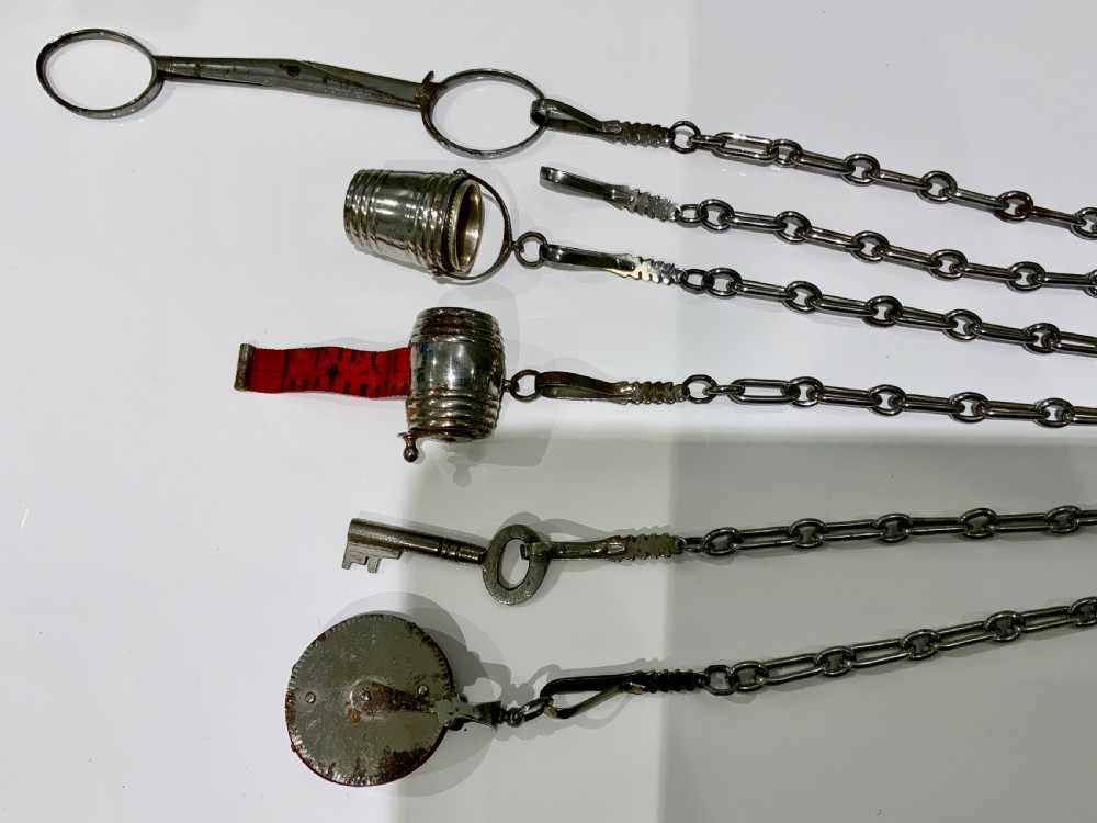 A nineteenth-century steel chatelaine featuring an ornamental waist clip and five suspended chains holding sewing tools, a key, a thimble, and a tape measure. View IV