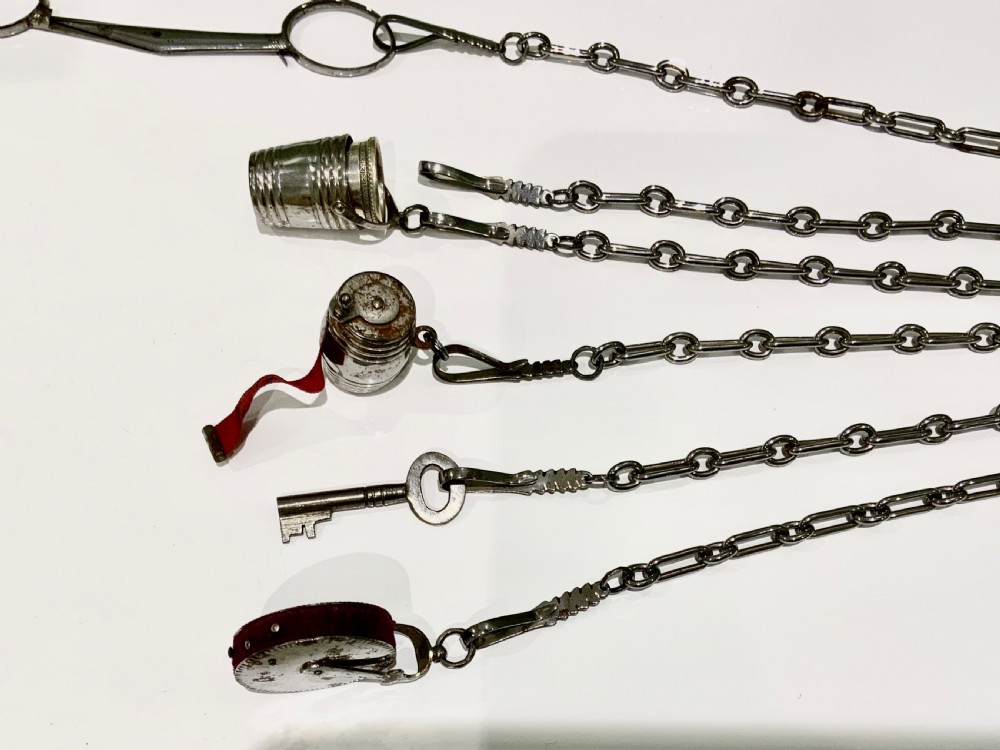 A nineteenth-century steel chatelaine featuring an ornamental waist clip and five suspended chains holding sewing tools, a key, a thimble, and a tape measure. View VI