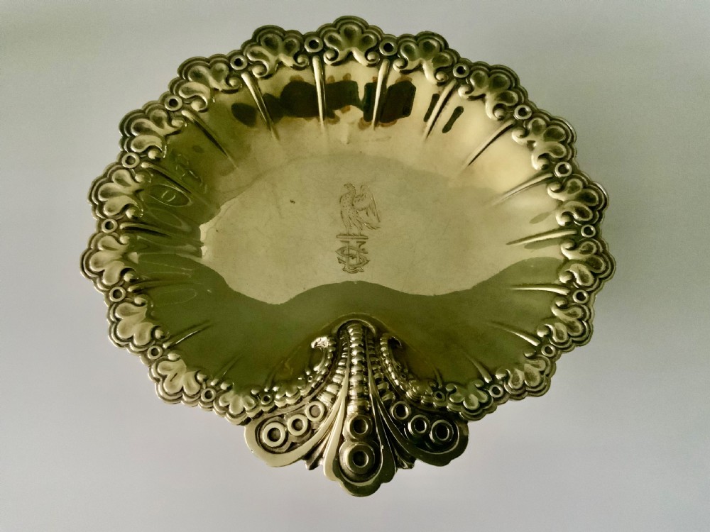 A Victorian shell-shaped silver-gilt dish with lobed fluting, a scalloped scroll rim, and an engraved crest at the centre.