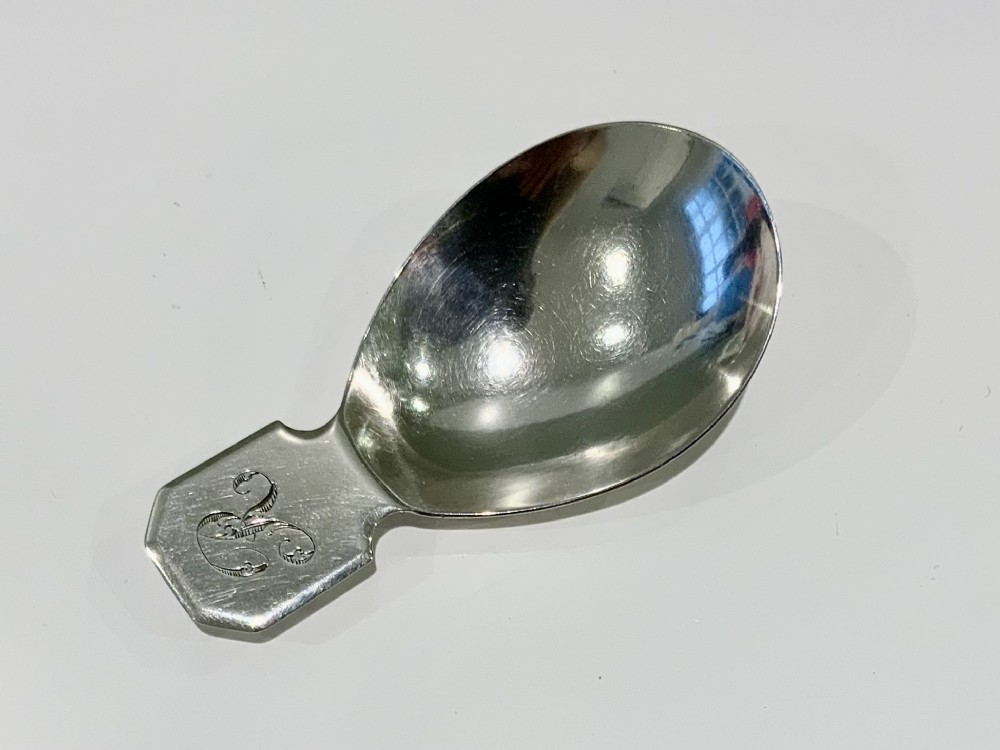 A Georgian sterling silver caddy spoon with a broad oval bowl and a short flat handle featuring engraved initials.