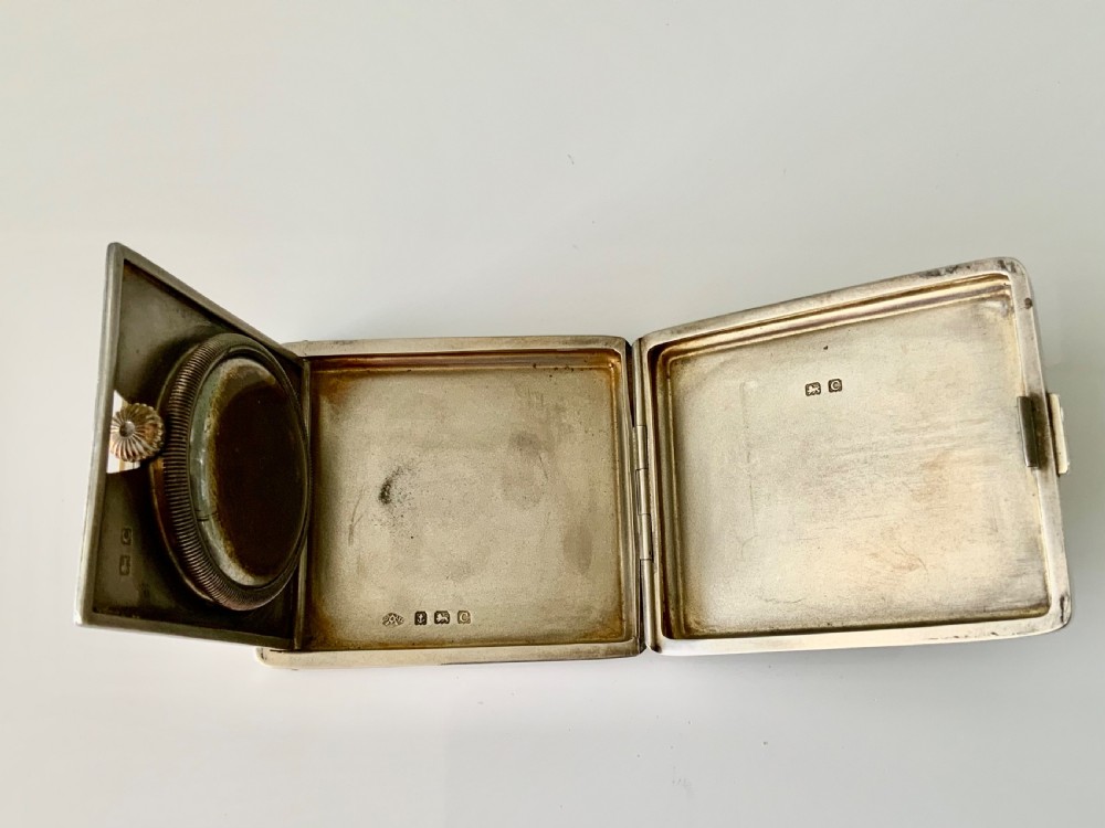 A square Art Deco silver travel clock featuring an engine-turned hinged case, brass bezel, and cream dial with gold Arabic numerals. View IV