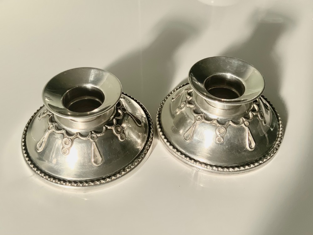A pair of circular silver travelling candlesticks with flared nozzles and decorative beaded and teardrop filigree motifs along the conical bases.