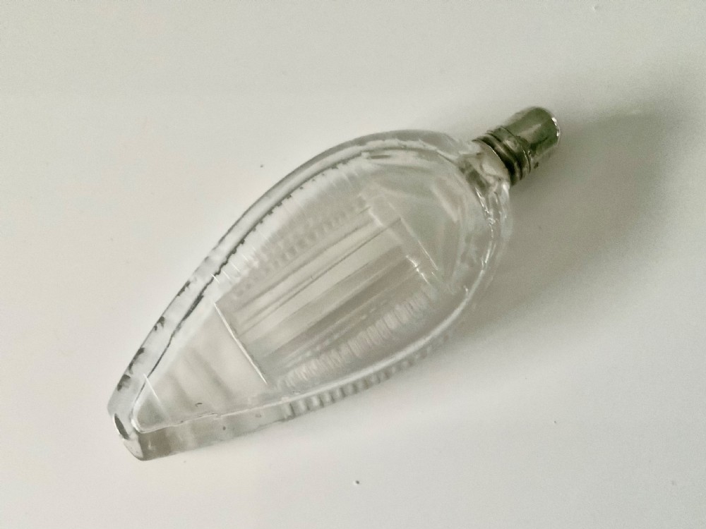 A teardrop-shaped clear glass scent bottle with a silver cap resting inside an open red leather plush-lined case. View III