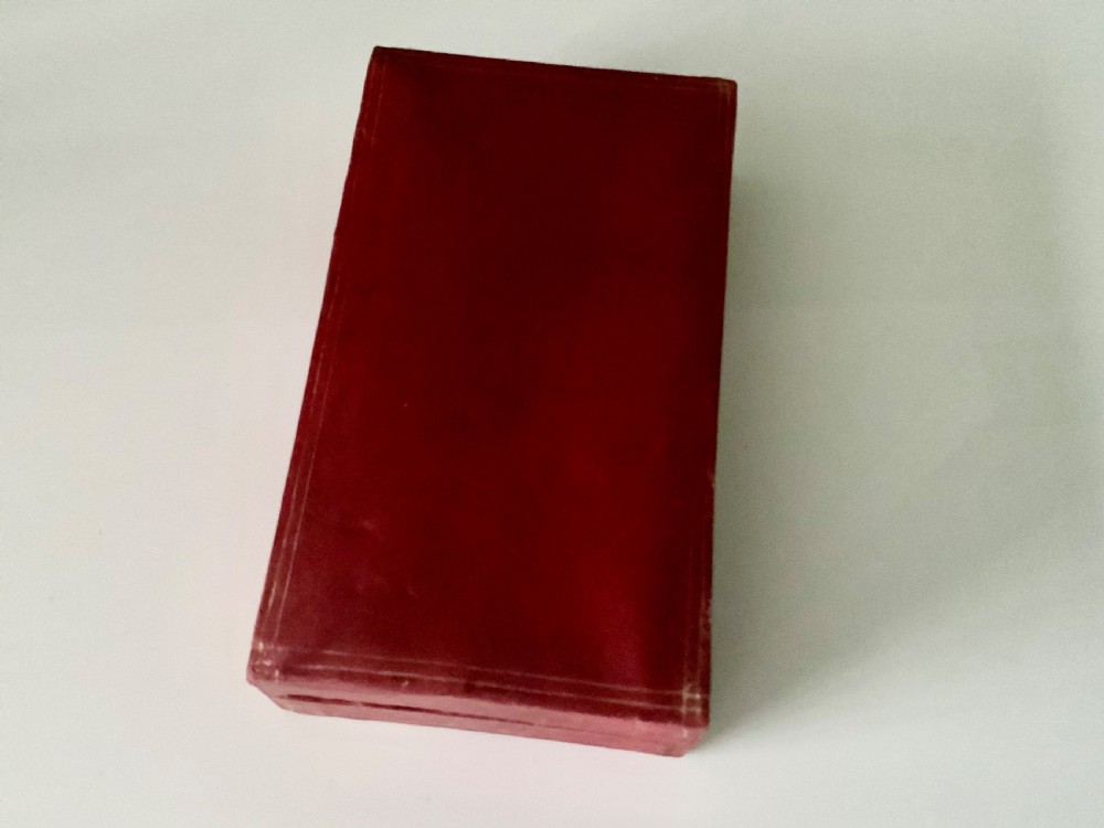 A teardrop-shaped clear glass scent bottle with a silver cap resting inside an open red leather plush-lined case. View V