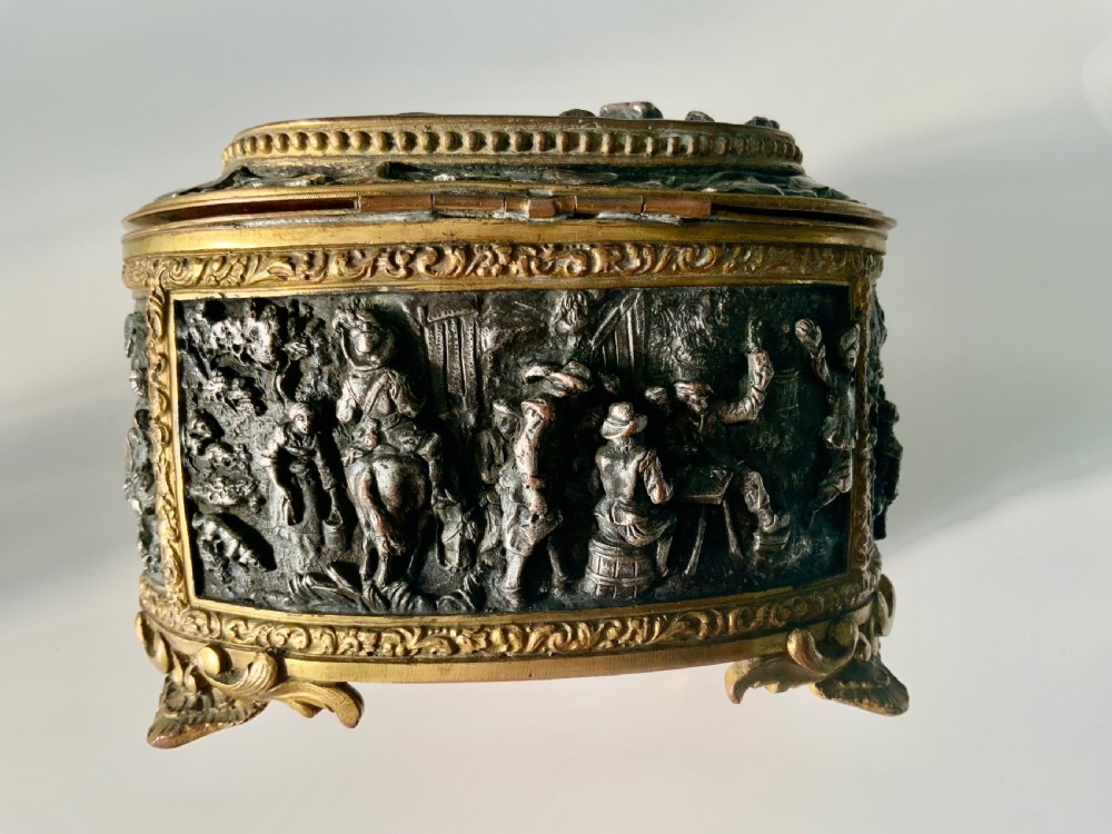 An oval antique French metal casket featuring relief panels of figures on horseback and cherubs holding an escutcheon with a key. View IV