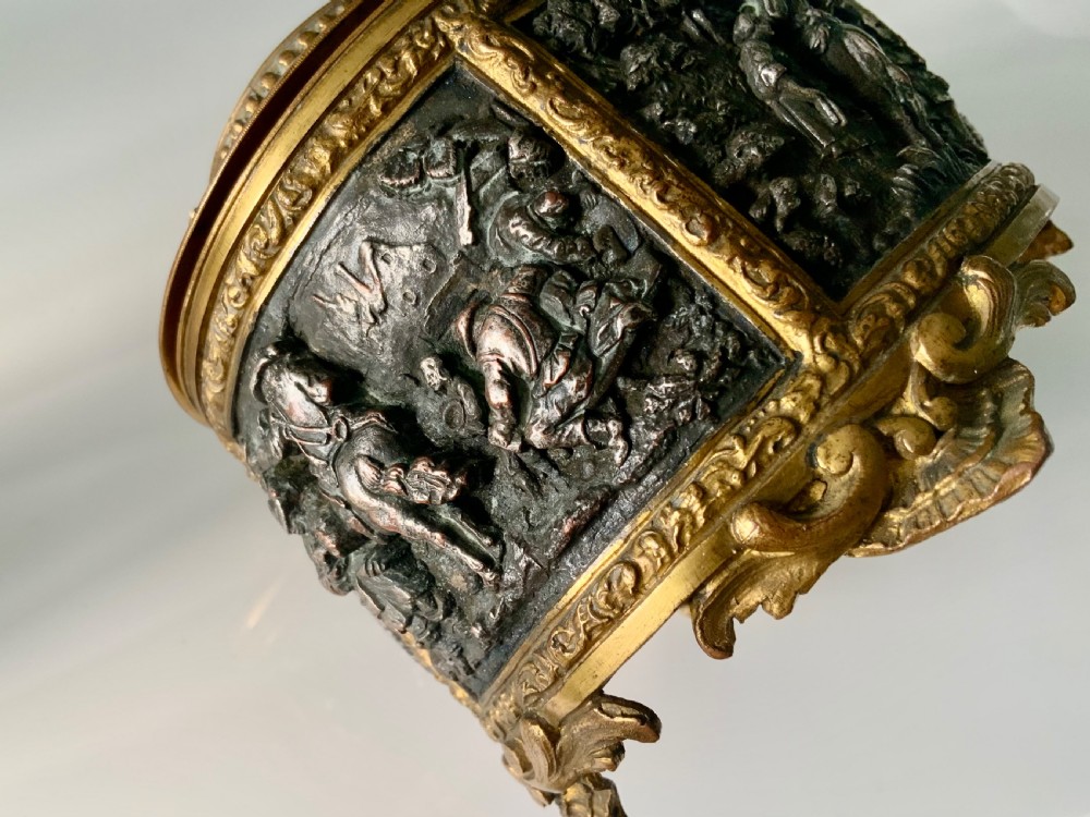 An oval antique French metal casket featuring relief panels of figures on horseback and cherubs holding an escutcheon with a key. View V