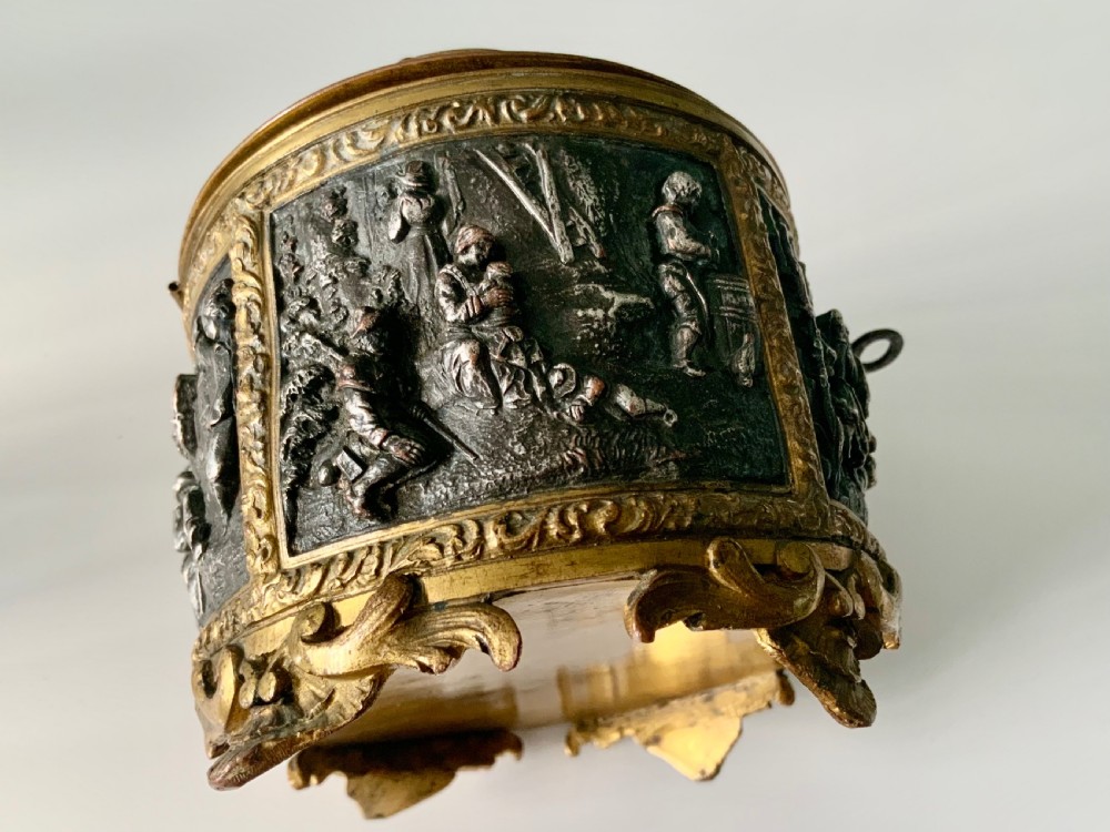 An oval antique French metal casket featuring relief panels of figures on horseback and cherubs holding an escutcheon with a key. View VI