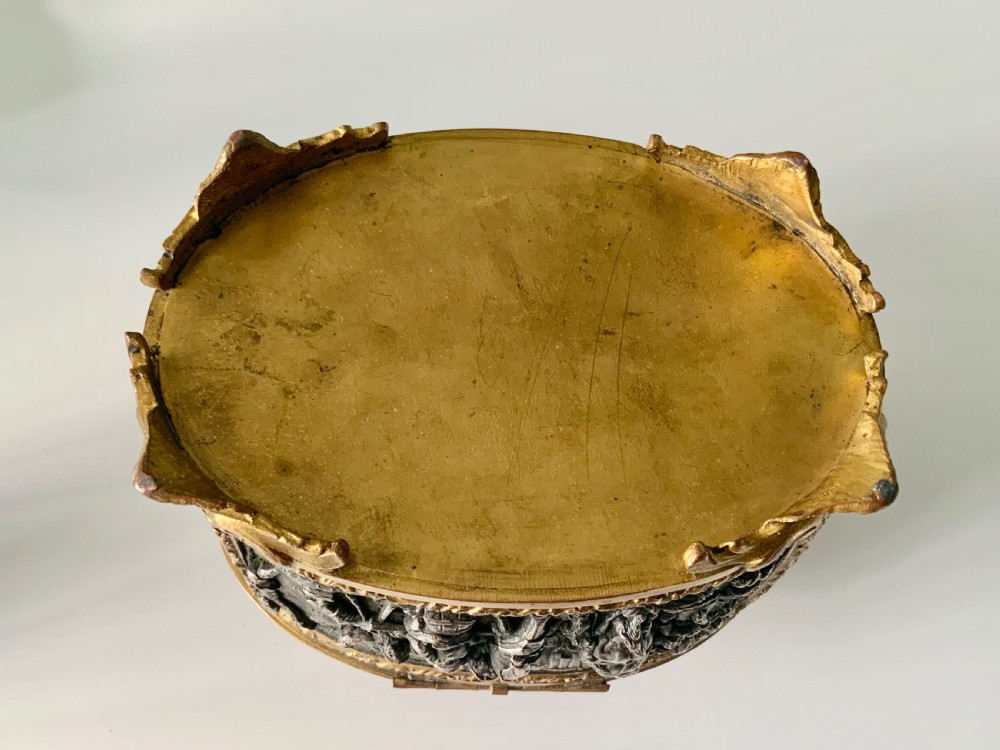 An oval antique French metal casket featuring relief panels of figures on horseback and cherubs holding an escutcheon with a key. View VII