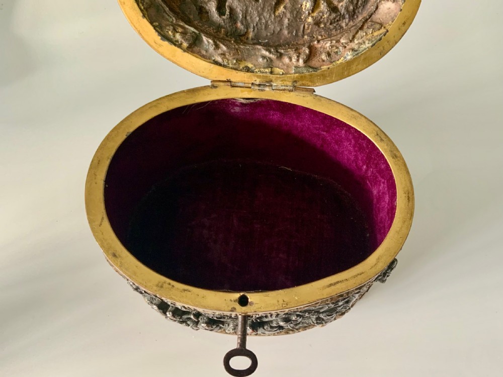 An oval antique French metal casket featuring relief panels of figures on horseback and cherubs holding an escutcheon with a key. View VIII