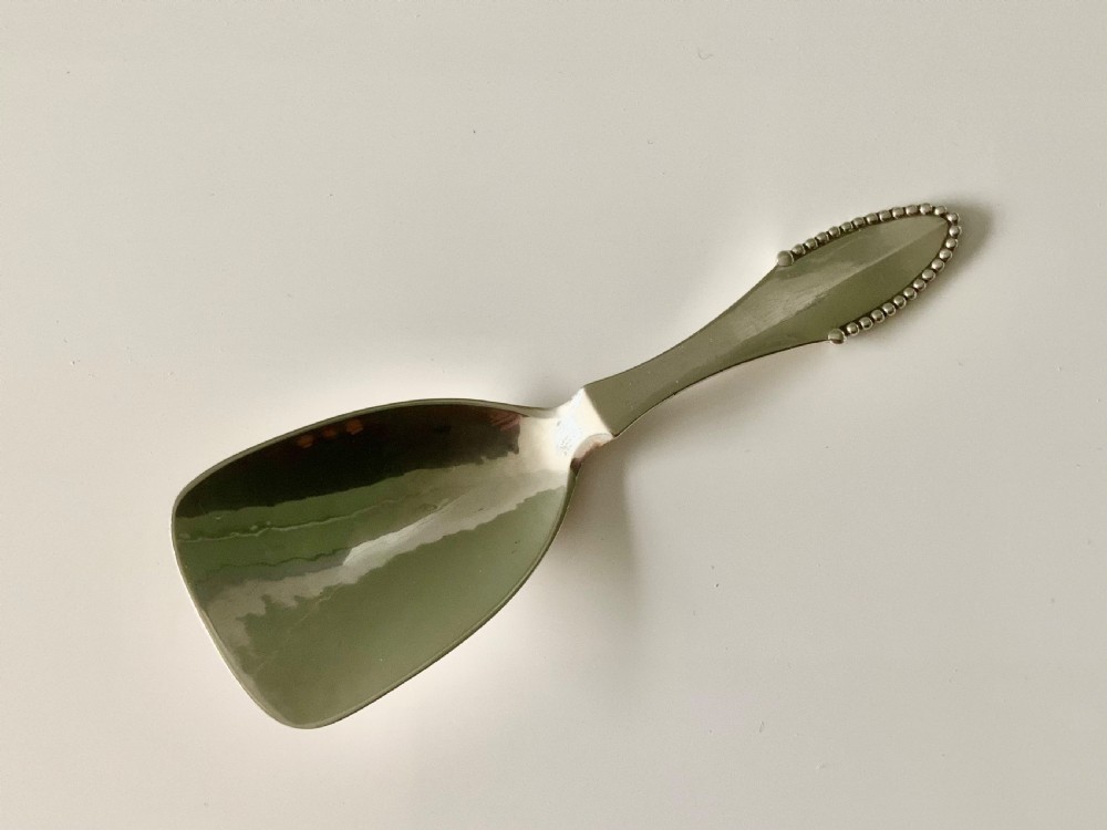A sterling silver caddy spoon featuring a wide shovel-shaped bowl and a tapered handle trimmed with beaded detailing.