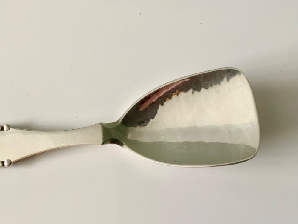 A sterling silver caddy spoon featuring a wide shovel-shaped bowl and a tapered handle trimmed with beaded detailing. View II