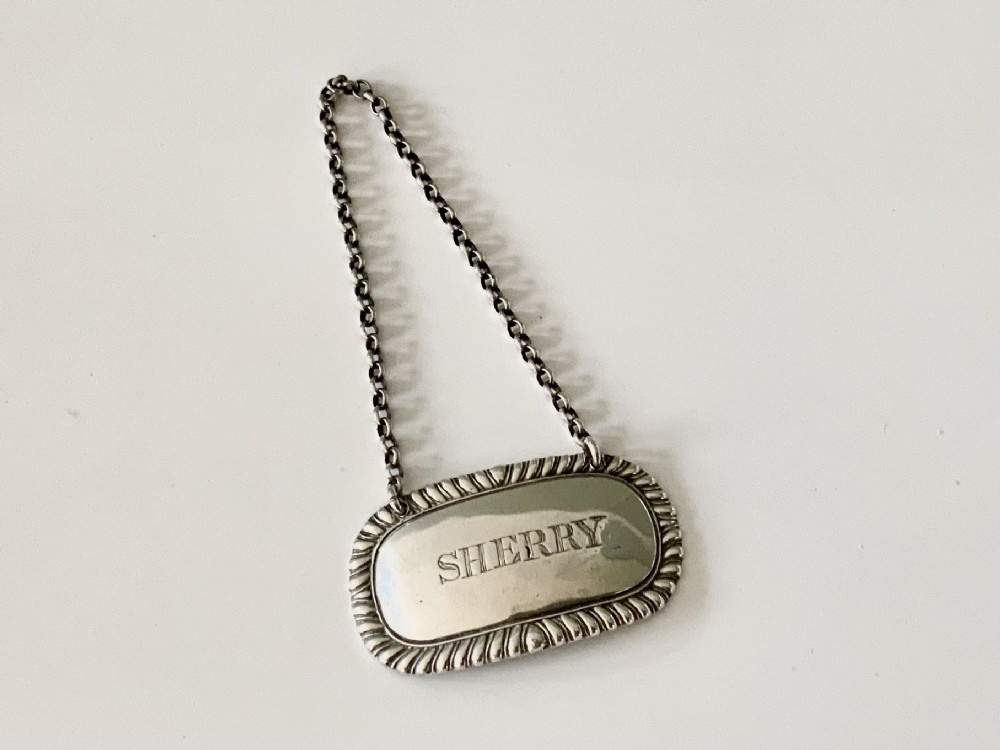 An oval Georgian silver decanter label engraved with SHERRY, complete with a gadrooned border and suspension chain.