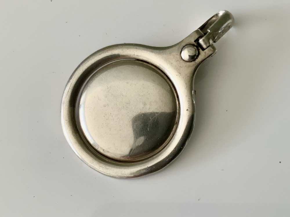 A circular silver napkin clip featuring a hinged spring mechanism and polished surface rests against a neutral white background.