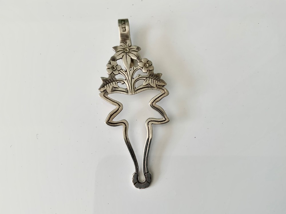 An antique silver napkin clip featuring floral repousse ornamentation and a top hook stamped with a maker mark.