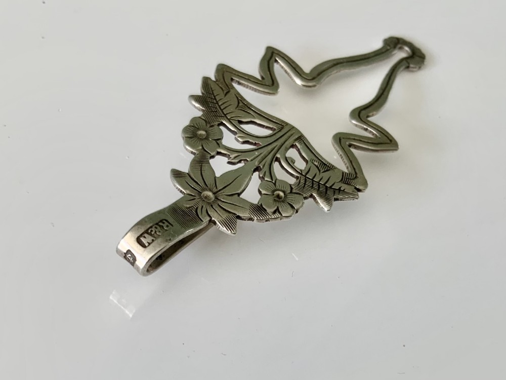 An antique silver napkin clip featuring floral repousse ornamentation and a top hook stamped with a maker mark. View III