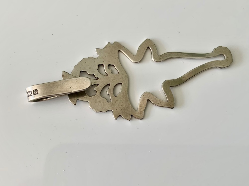 An antique silver napkin clip featuring floral repousse ornamentation and a top hook stamped with a maker mark. View IV