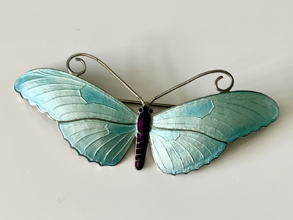 A silver butterfly brooch with turquoise guilloche enamel wings, dark purple central body, and wire antennae.
