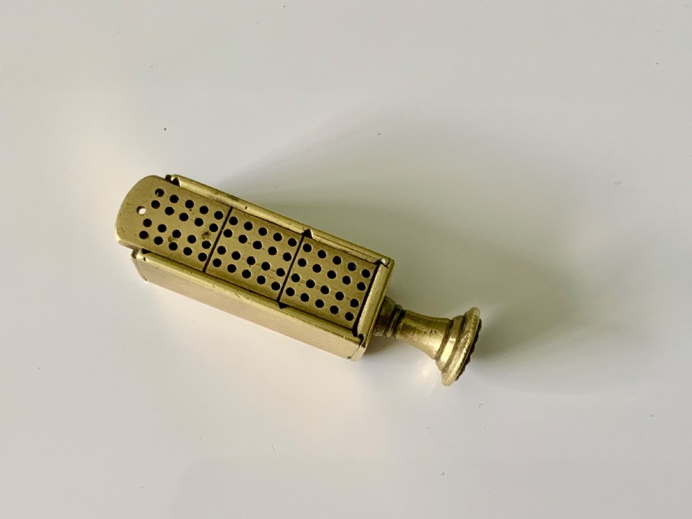 A nineteenth-century cast brass pipe tamper featuring a rectangular miniature cribbage scoring board connected to a turned pedestal handle.