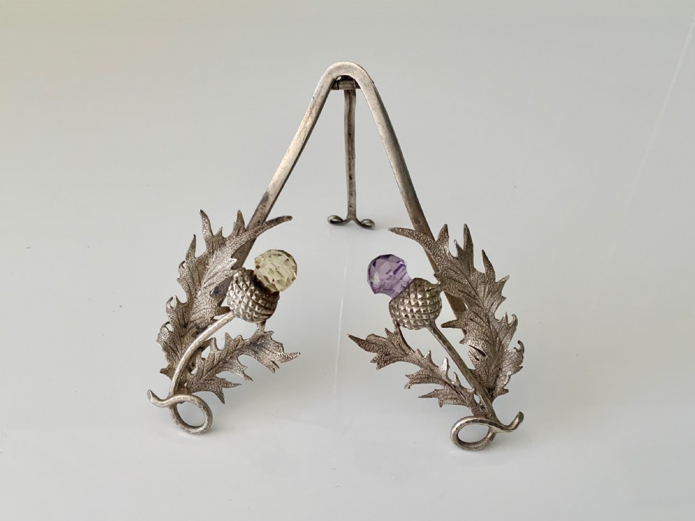 An easel-backed silver menu holder featuring detailed Scottish thistle leaves and two thistle heads set with faceted purple and yellow stones.