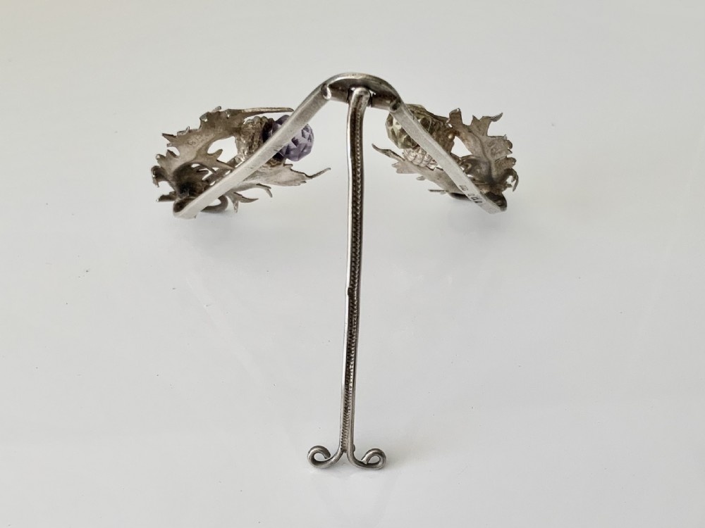 An easel-backed silver menu holder featuring detailed Scottish thistle leaves and two thistle heads set with faceted purple and yellow stones. View II