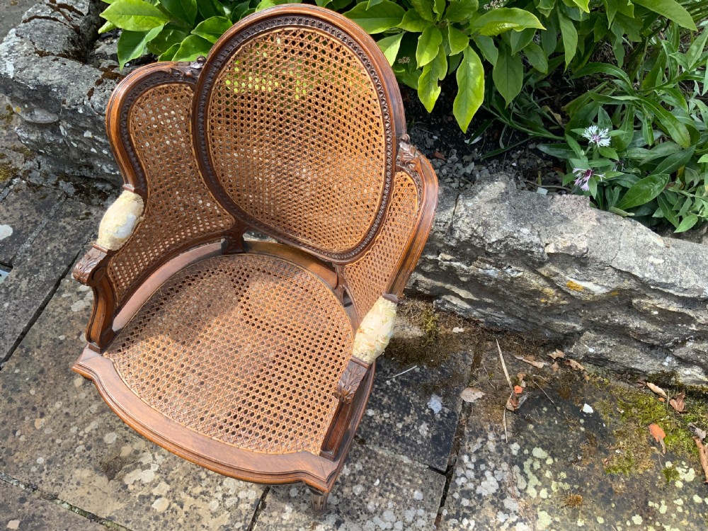 A 19th-century childs bergere chair crafted from carved brown wood with woven rattan cane panels on the oval back, sides, and seat. View III
