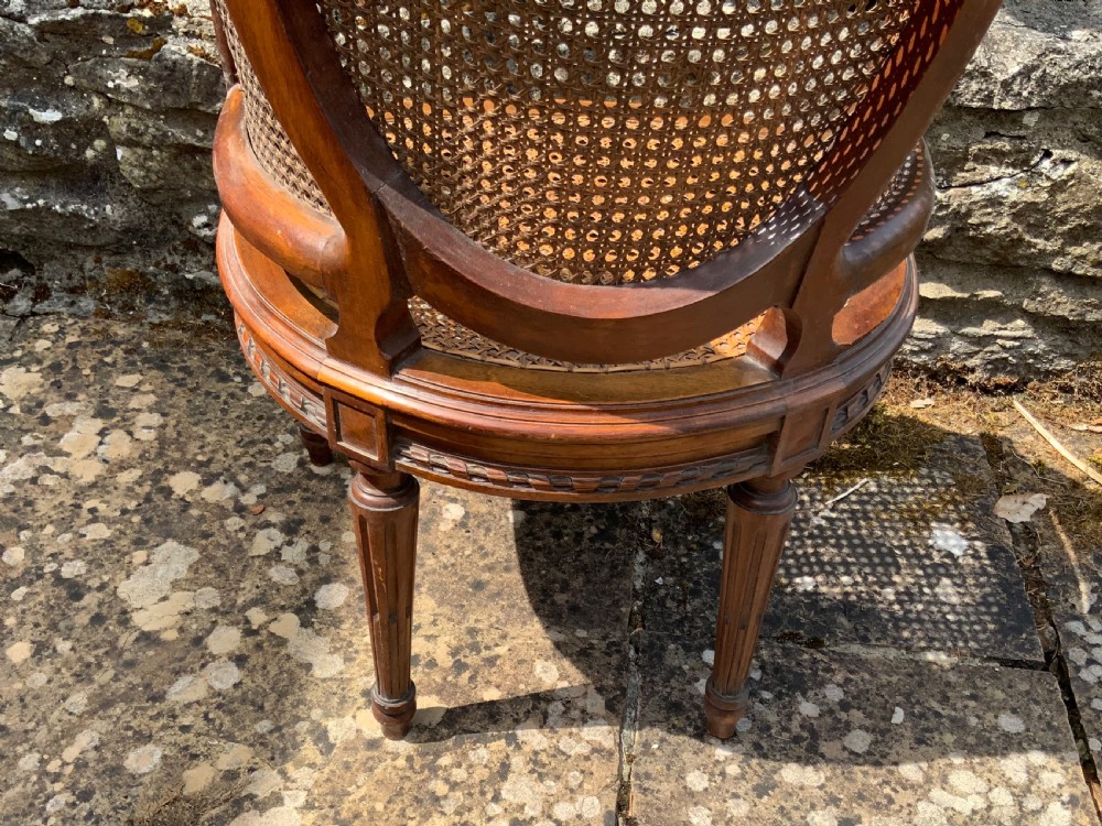 A 19th-century childs bergere chair crafted from carved brown wood with woven rattan cane panels on the oval back, sides, and seat. View VIII