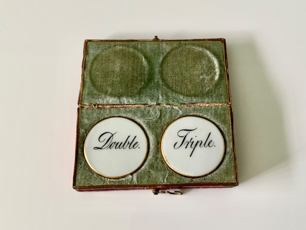 A set of four round white porcelain whist counters featuring suit motifs alongside a red gilt-tooled leather storage box. View III