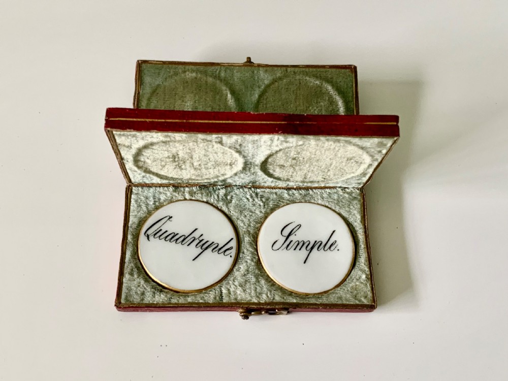 A set of four round white porcelain whist counters featuring suit motifs alongside a red gilt-tooled leather storage box. View V