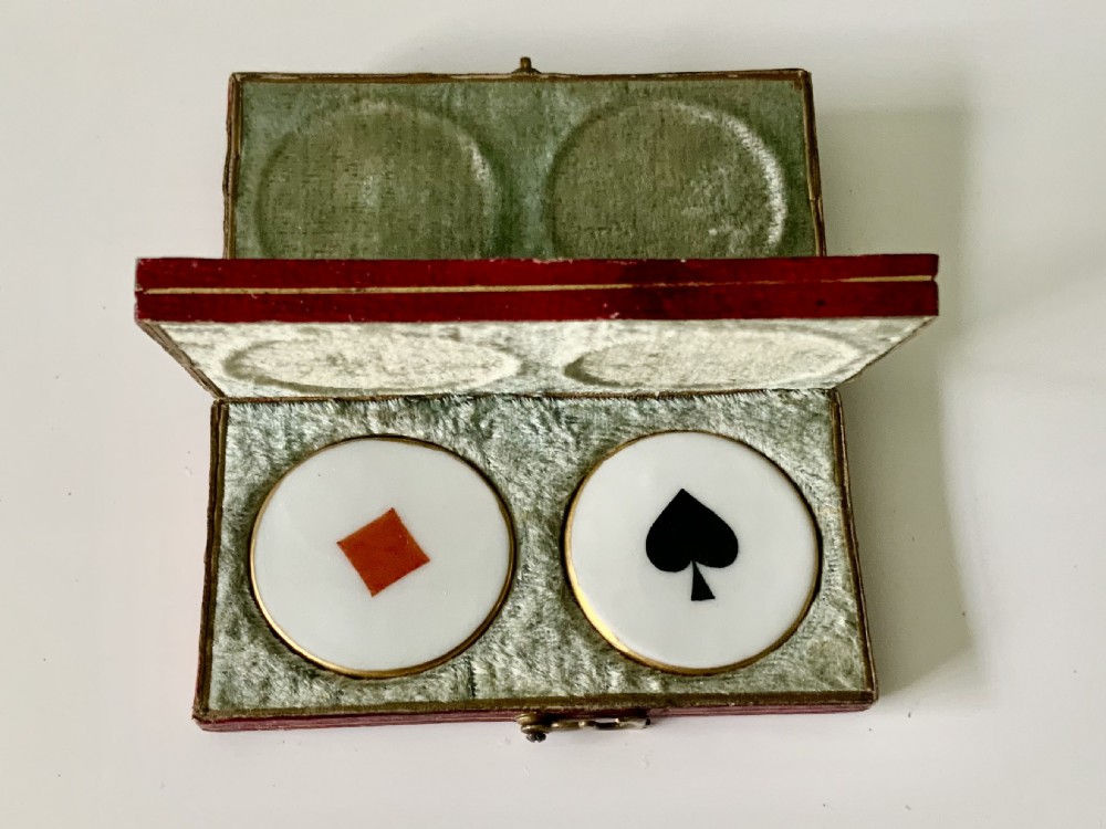 A set of four round white porcelain whist counters featuring suit motifs alongside a red gilt-tooled leather storage box. View VI