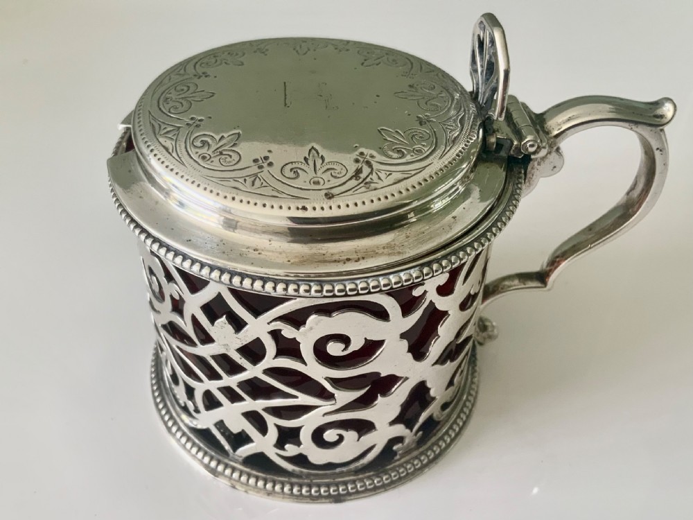 A pierced silver mustard pot with an engraved hinged lid, beaded rims, and a visible ruby red glass liner. View IV