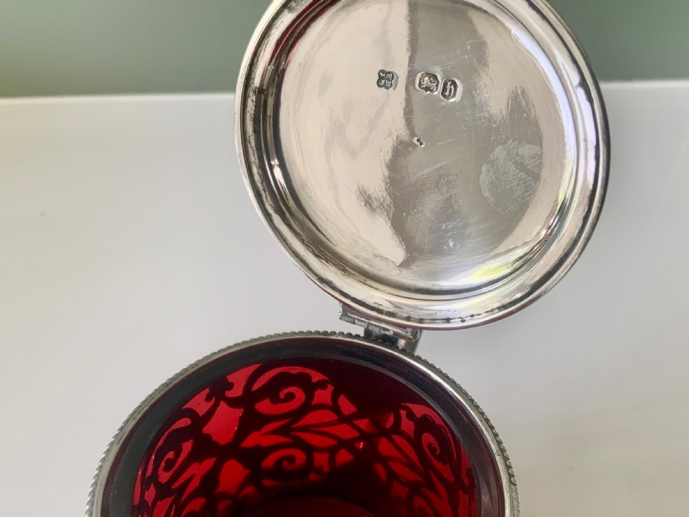 A pierced silver mustard pot with an engraved hinged lid, beaded rims, and a visible ruby red glass liner. View V
