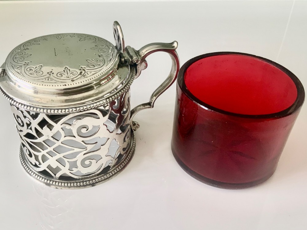 A pierced silver mustard pot with an engraved hinged lid, beaded rims, and a visible ruby red glass liner. View VIII
