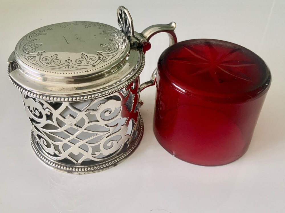 A pierced silver mustard pot with an engraved hinged lid, beaded rims, and a visible ruby red glass liner. View IX