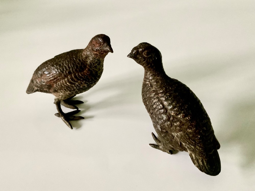 A pair of small, detailed cold-painted bronze figures depicting standing grouse birds with textured feathering.