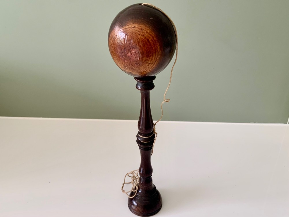 A lathe-turned dark wood bilboquet featuring a slender stem, attached cord, and a polished wooden sphere resting atop the spindle.