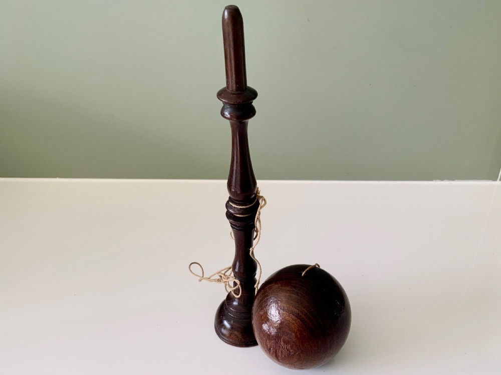 A lathe-turned dark wood bilboquet featuring a slender stem, attached cord, and a polished wooden sphere resting atop the spindle. View II